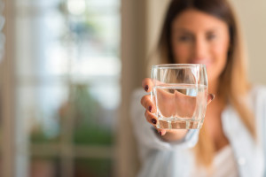 Beautiful young woman smiling while holding a glass of water at home. Lifestyle concept.